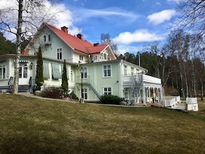 A large, light green building with a red roof, multiple windows, and a covered porch area.