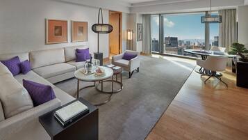 A modern living room with a sofa, coffee table, and chairs, a dining area with a table and chairs, and a large window offering a city view.