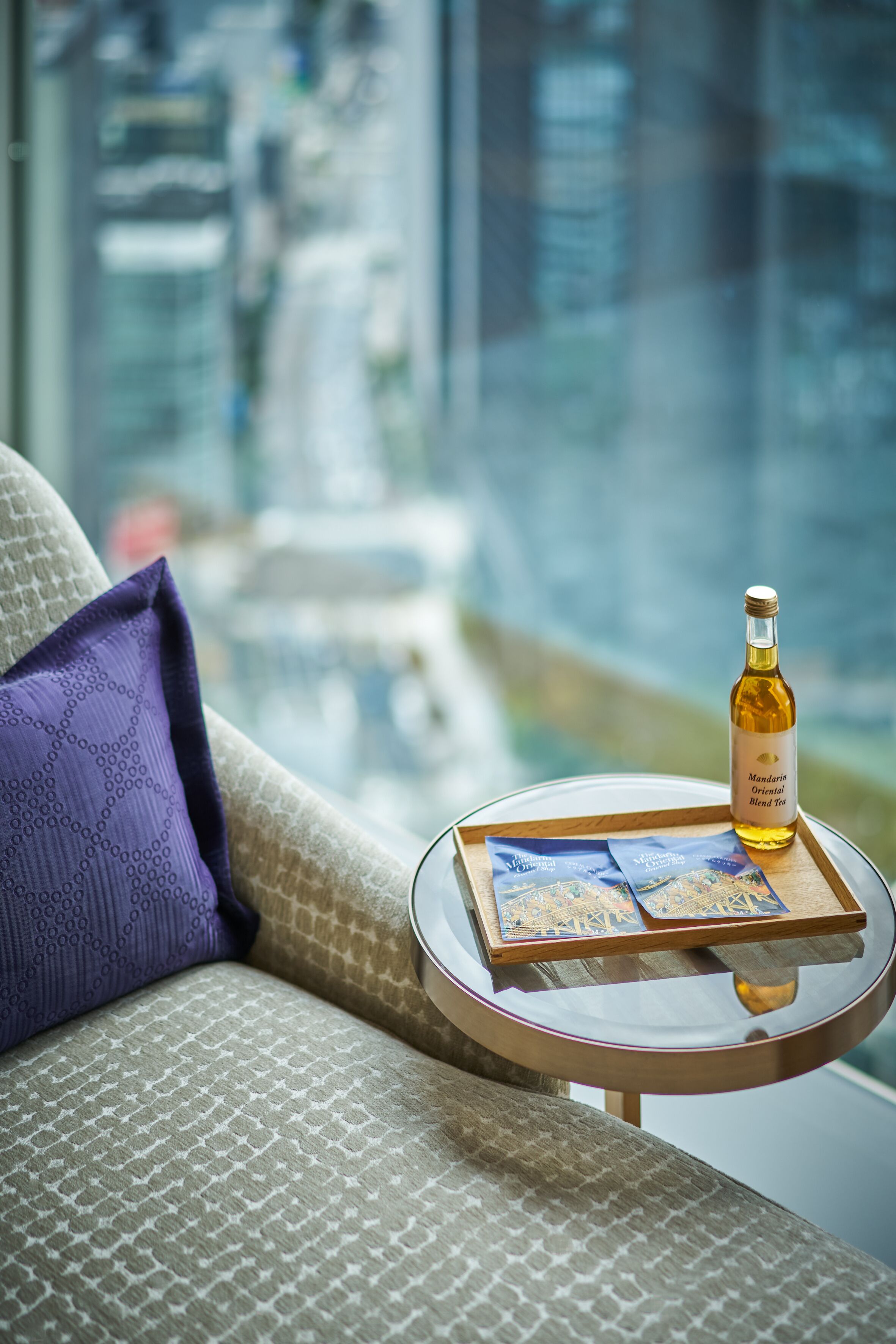 Una mesa de vidrio con una botella de Té Oriental y bolsitas de té sobre un sofá acolchado con un cojín morado.