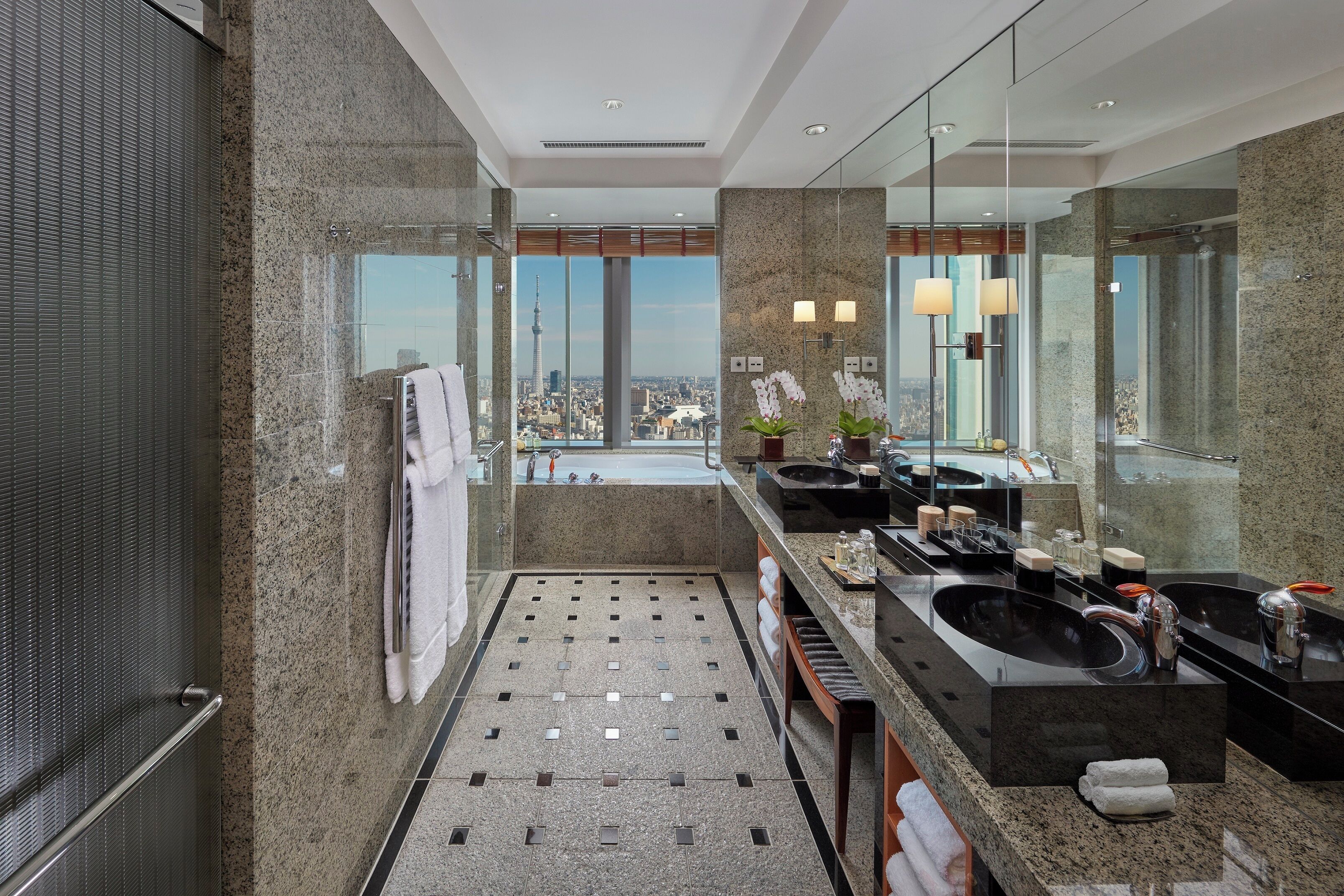 Un baño moderno con un espejo grande, dos lavamanos, una bañera y vistas a la ciudad.