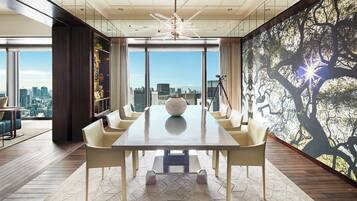 A modern dining area with a large table, multiple chairs, and a city view through large windows.