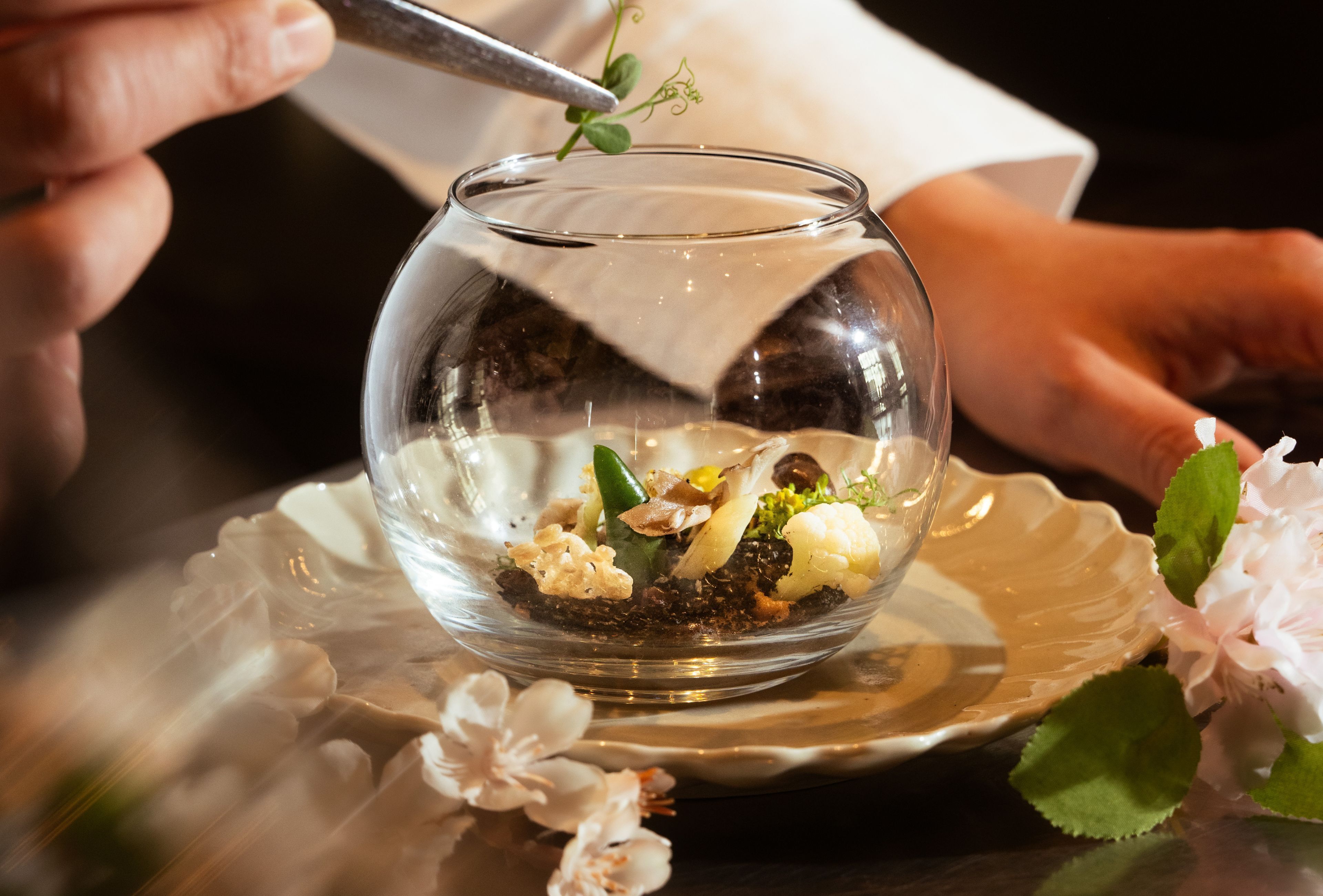 Un tazón de vidrio transparente con un postre sobre un plato decorativo, rodeado de flores.