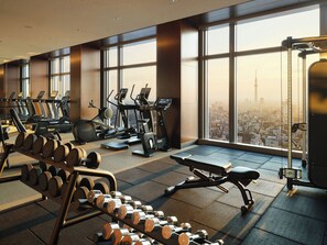 Un gimnasio con cintas de correr, elípticas y pesas libres, con amplios ventanales y vistas a la ciudad.