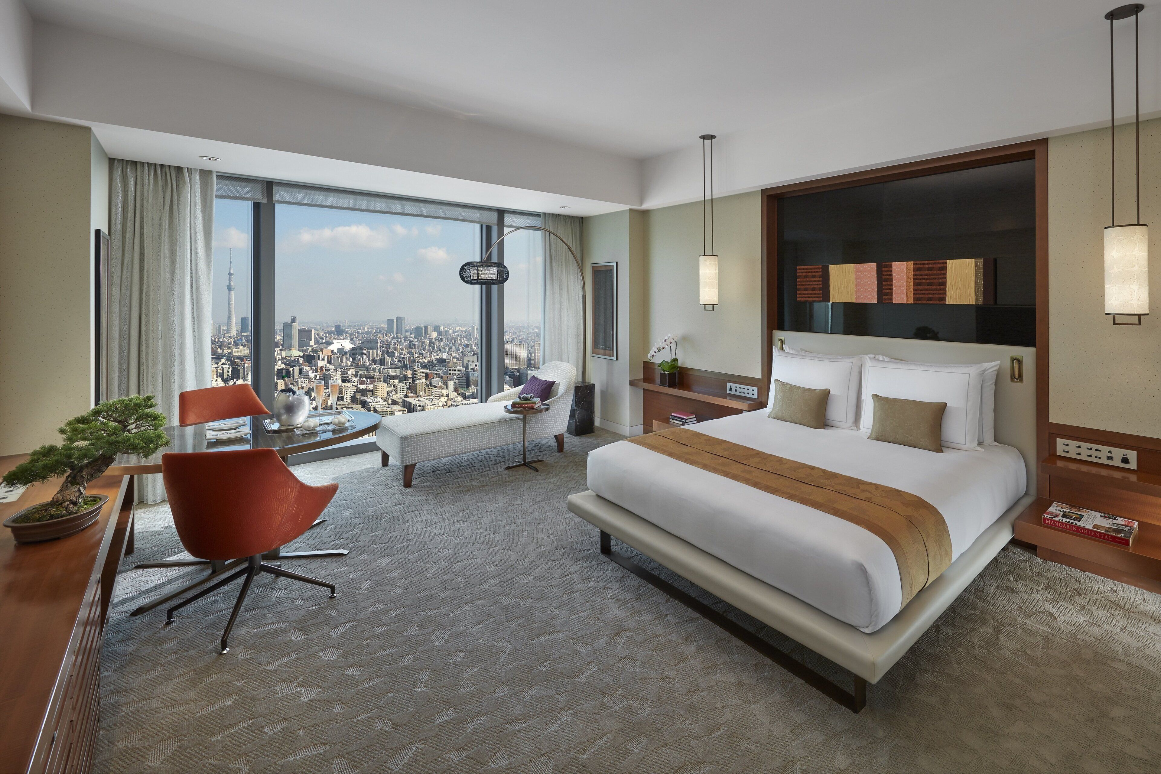 Une chambre d’hôtel avec un grand lit, un bureau, une chaise, une petite table, une plante en pot et une vue sur le paysage urbain.