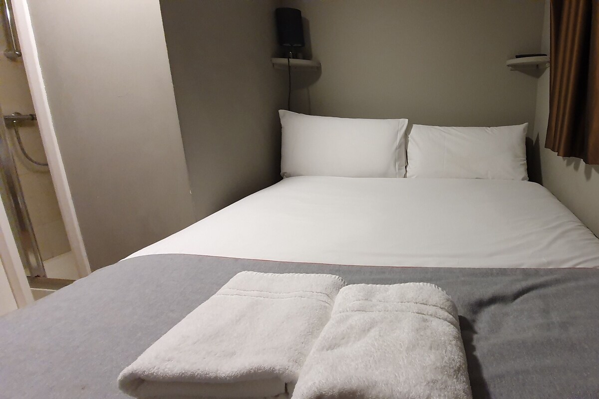 A single bed with white linens, a grey blanket, and two white towels.