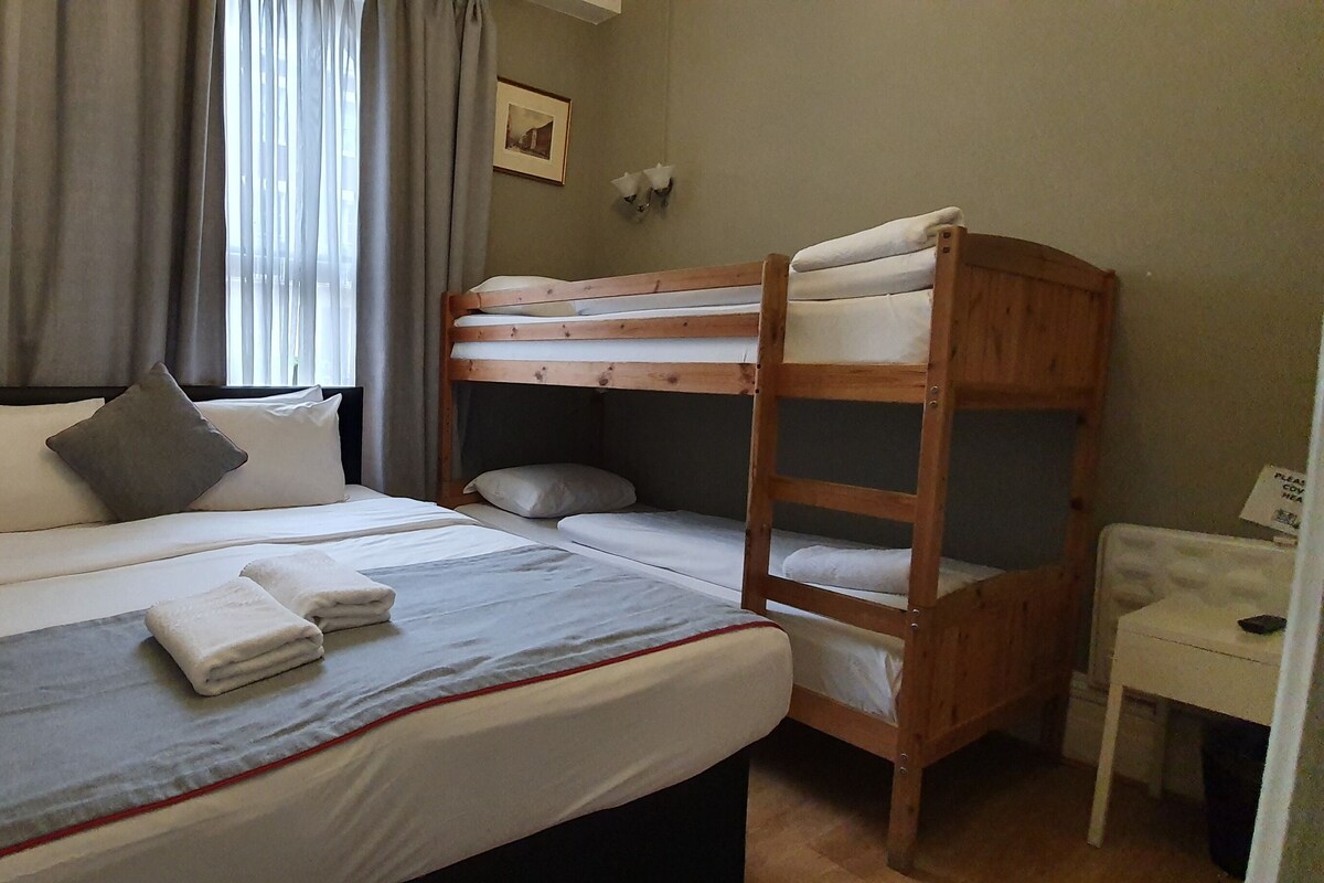 A bedroom with a bunk bed, a bedside table with a lamp, a chair, and a shelf with hangers.