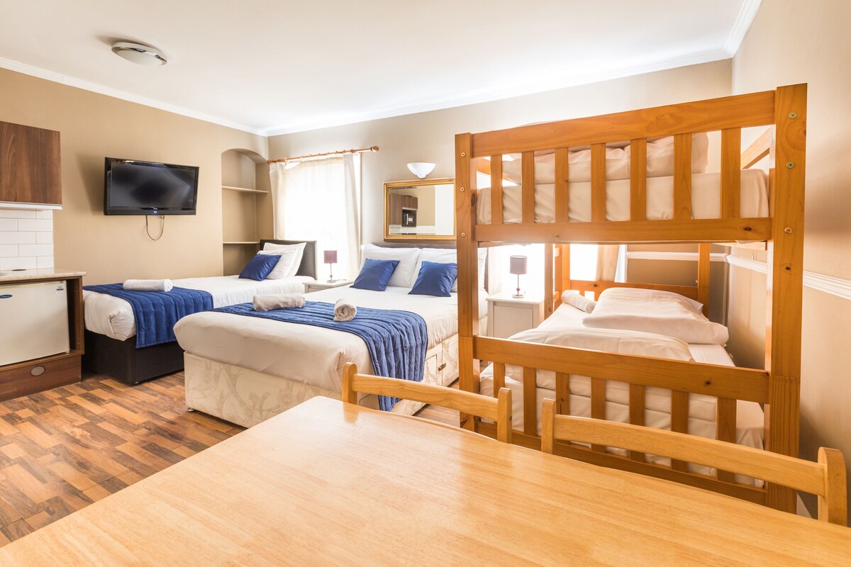 A hotel room with bunk beds, a desk, a television, and a bathroom.