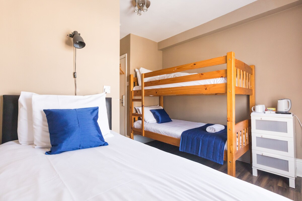 A room with a bunk bed, a bedside table with a lamp, and a dresser.
