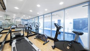 A modern gym with cardio machines, a mirrored wall, and large windows overlooking a snowy landscape.