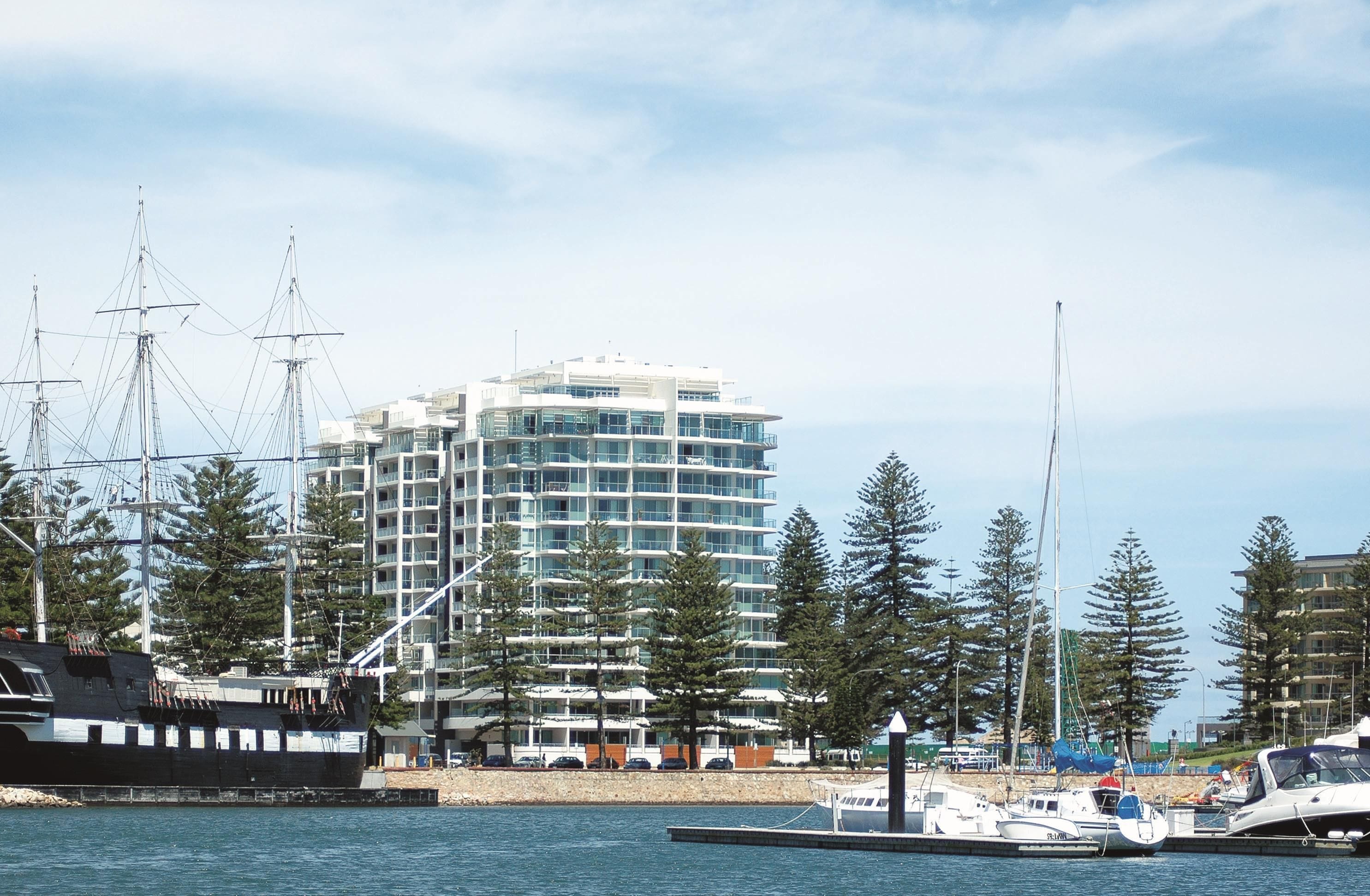A marina with a tall building in the background, boats docked, and a clear sky.