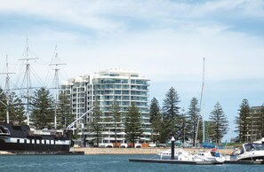 A marina with a tall building in the background, boats docked, and a clear sky. - Oaks Glenelg Liberty Suites (Glenelg)