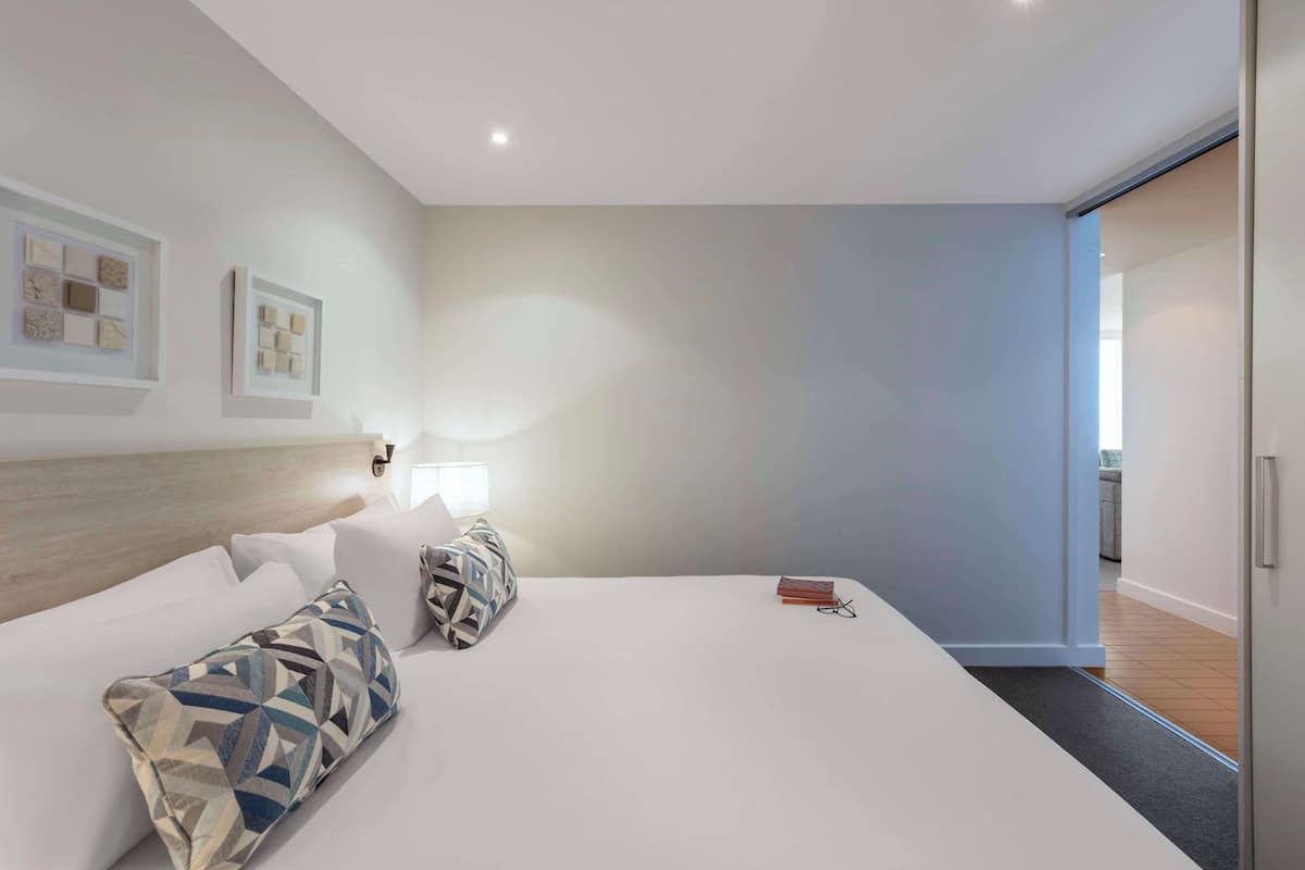 Une chambre d’hôtel moderne avec un grand lit, deux oreillers, une table de chevet avec une lampe et des œuvres d’art encadrées accrochées au mur.