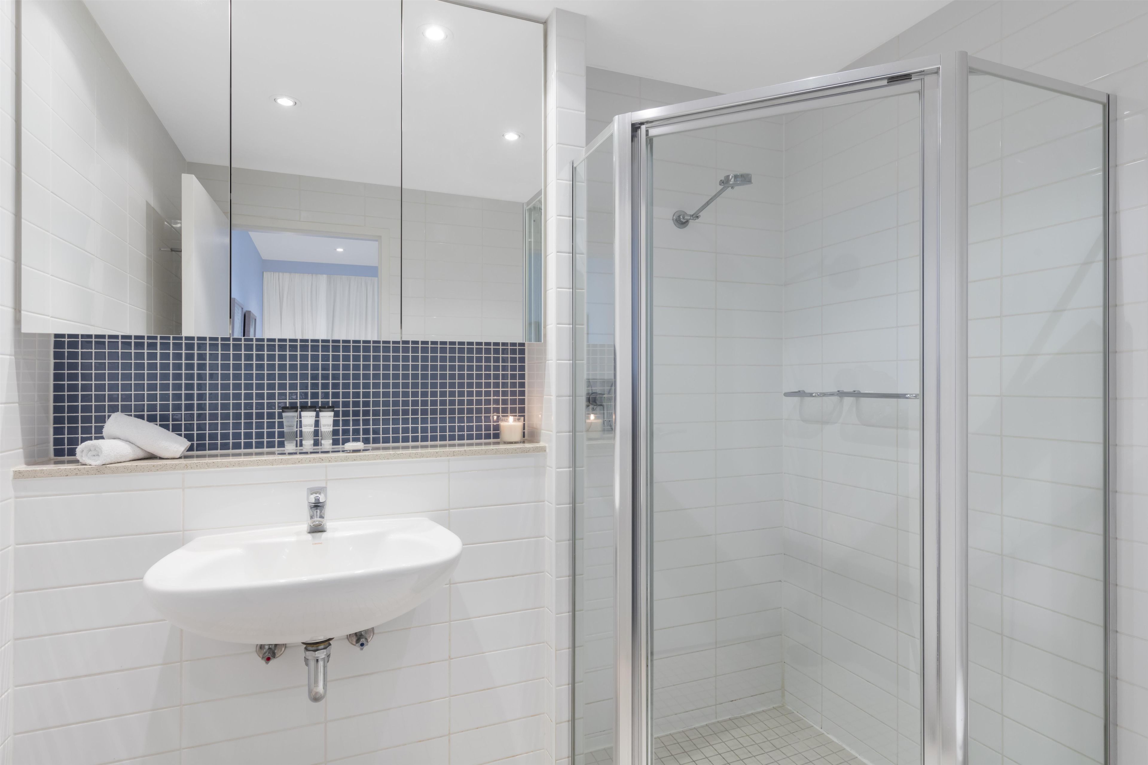 Une salle de bain avec un lavabo blanc, une cabine de douche en verre et un mur recouvert de carreaux bleus derrière le lavabo.