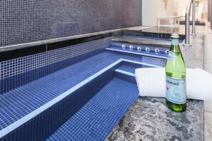 Una piscina de hidromasaje con interior de azulejos azules, una botella de agua y una toalla blanca sobre una superficie de piedra.