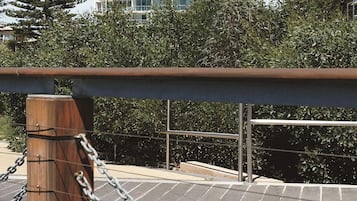 A chain-link fence with a wooden post and metal railing, overlooking a landscaped area with a building in the background.