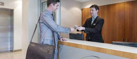 Two individuals exchanging a card at a reception desk in a modern office setting.