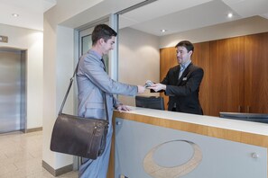 Two individuals exchanging a card at a reception desk in a modern office setting. - Oaks Glenelg Liberty Suites (Glenelg)