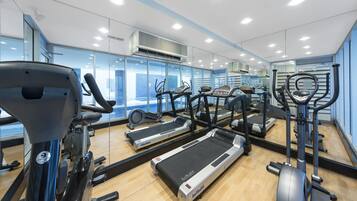Un gimnasio con cintas de correr, elípticas y un espejo grande.
