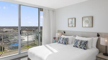 Een hotelkamer met een groot bed, twee wandlampen en uitzicht op een jachthaven.