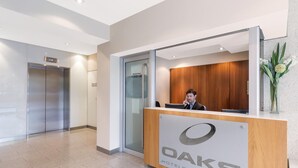 A reception desk with a logo, a man sitting behind it, and an elevator in the background. - Oaks Glenelg Liberty Suites (Glenelg)