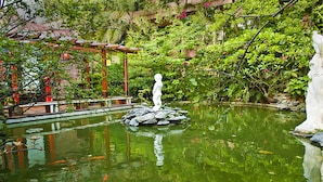 Un jardín tranquilo con un estanque, una estatua y abundante vegetación.