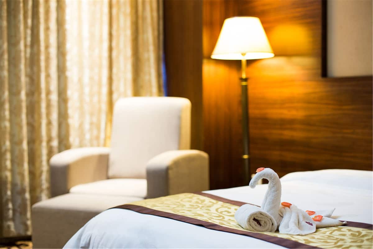 A hotel room with a bed, a lamp, a chair, and a swan towel decoration.
