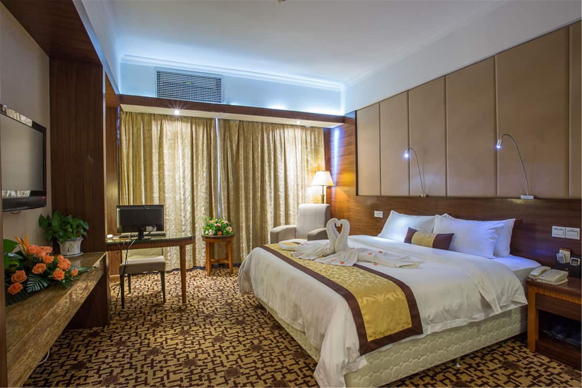 A hotel room with a large bed, a desk with a computer, a TV, and a lamp.