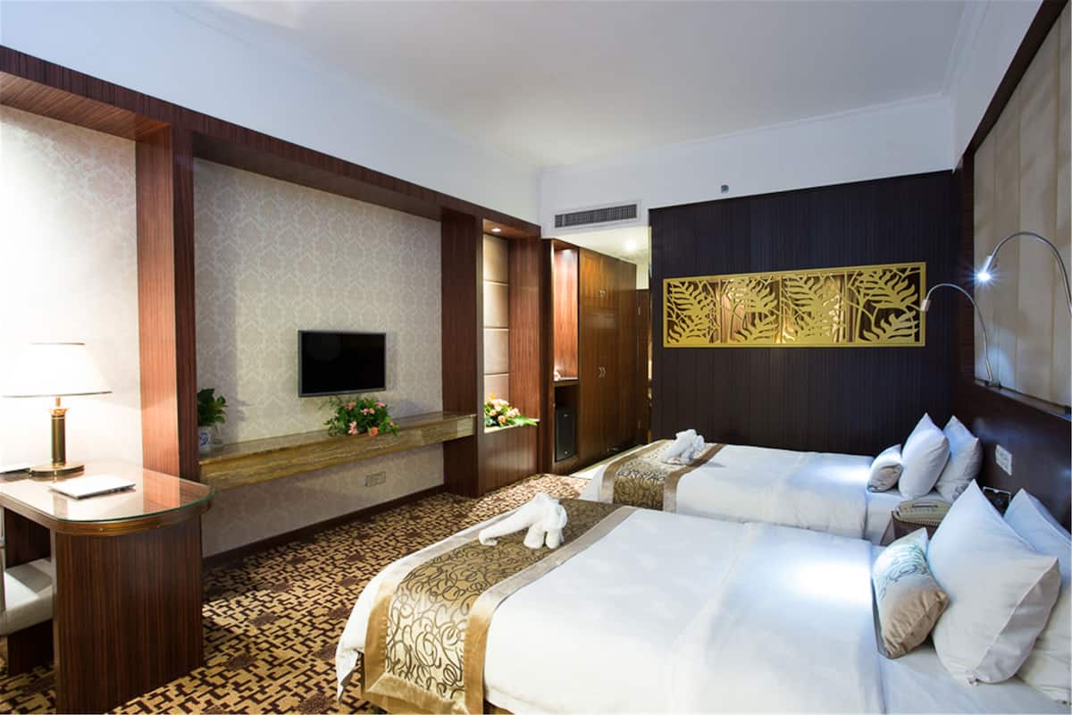A hotel room with two beds, a TV, a desk with a lamp, and a decorative wall panel.