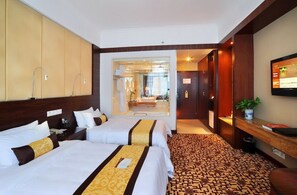 Habitación de hotel con dos camas, televisión, escritorio y baño visible a través de una puerta abierta.