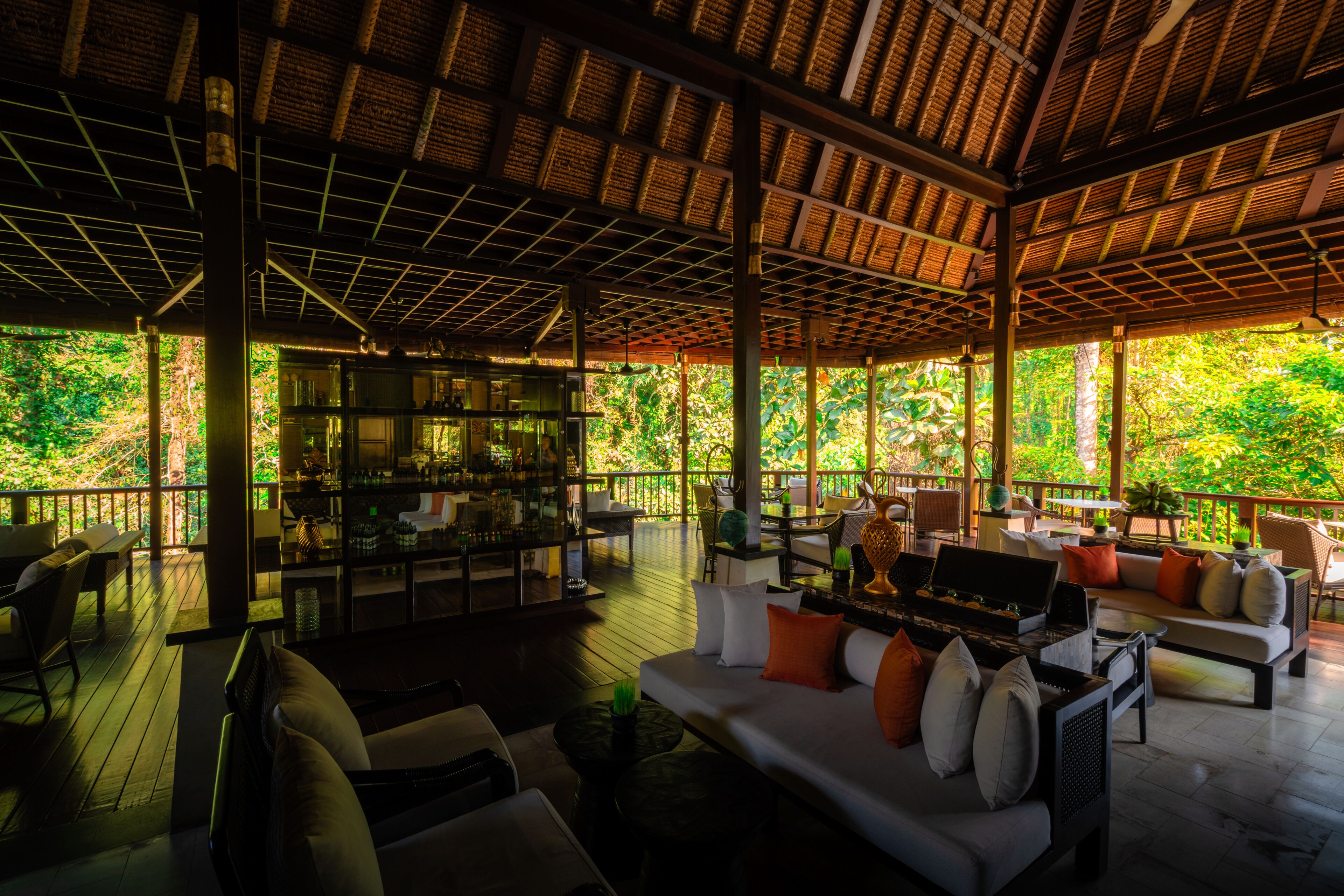 An indoor/outdoor lounge area with wooden flooring, seating arrangements, and a glass partition.