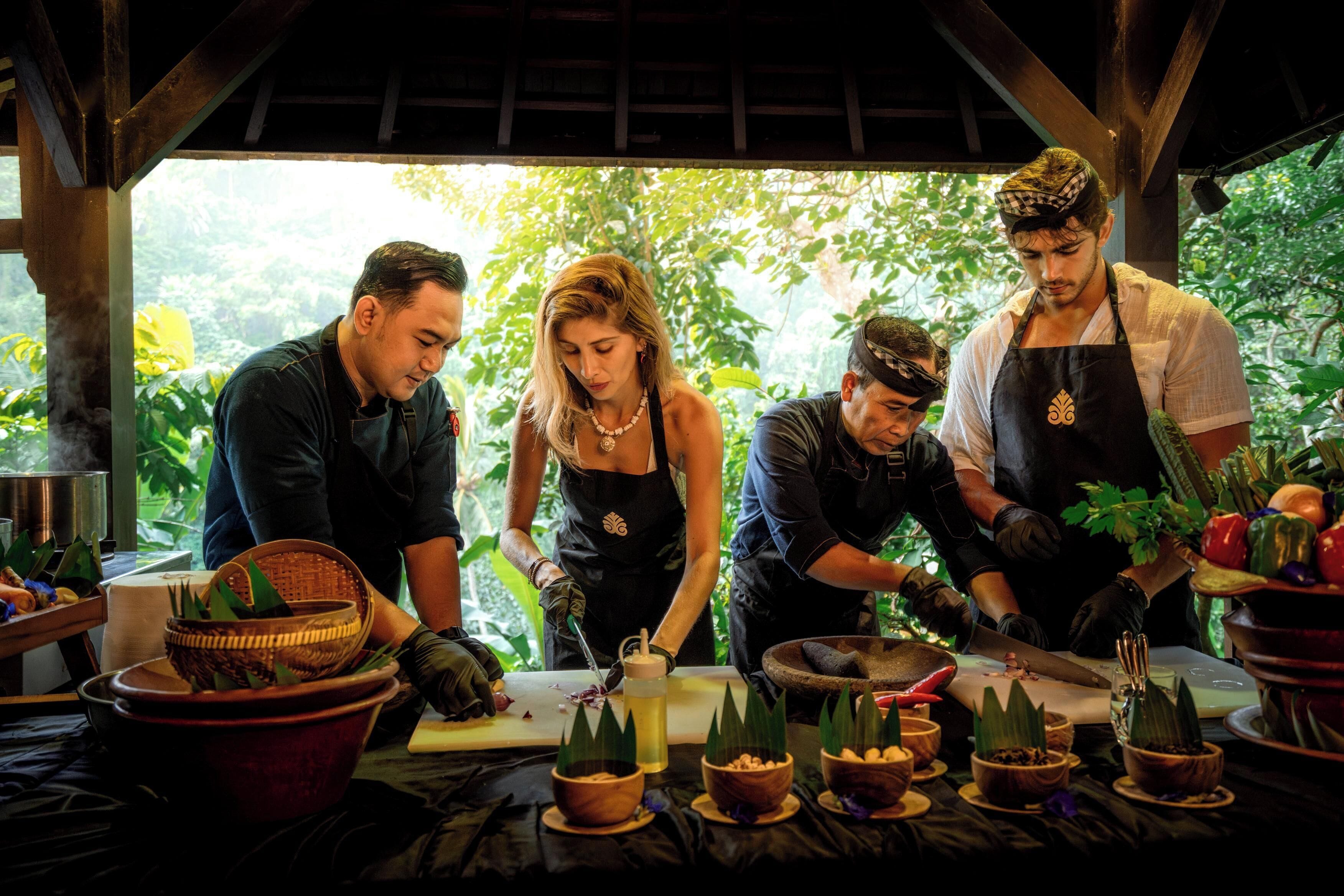 Un grupo de personas preparando comida al aire libre, rodeadas de utensilios de cocina y varios ingredientes.