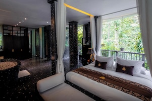 Une chambre d’hôtel avec un balcon, un lit agrémenté d’oreillers décoratifs, un coin salon avec une table ronde et une vue sur la verdure environnante.