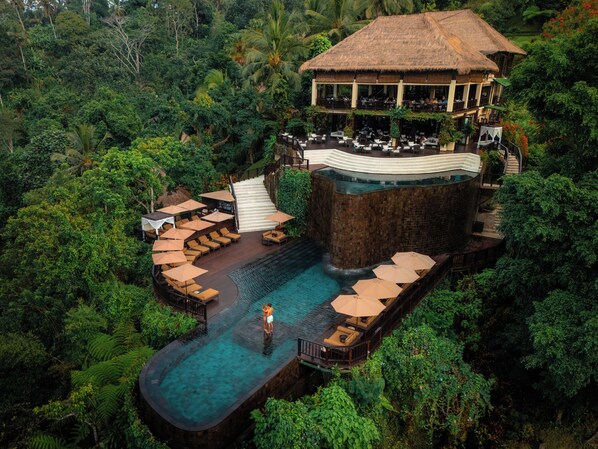 An aerial view of a resort with a pool, lounge areas, and a restaurant.