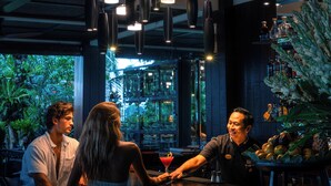 A bar area with hanging pendant lights, a bartender, and a customer.