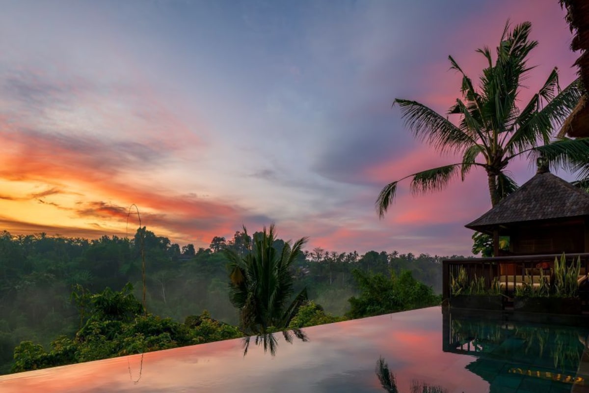 A infinity pool with a view of a sunset and palm trees.