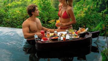 Una pareja cenando junto a una piscina con exuberante follaje de fondo.