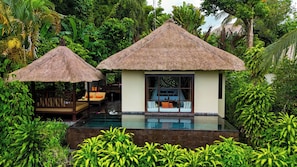 A resort with two thatched-roof structures, a pool, and lush greenery.