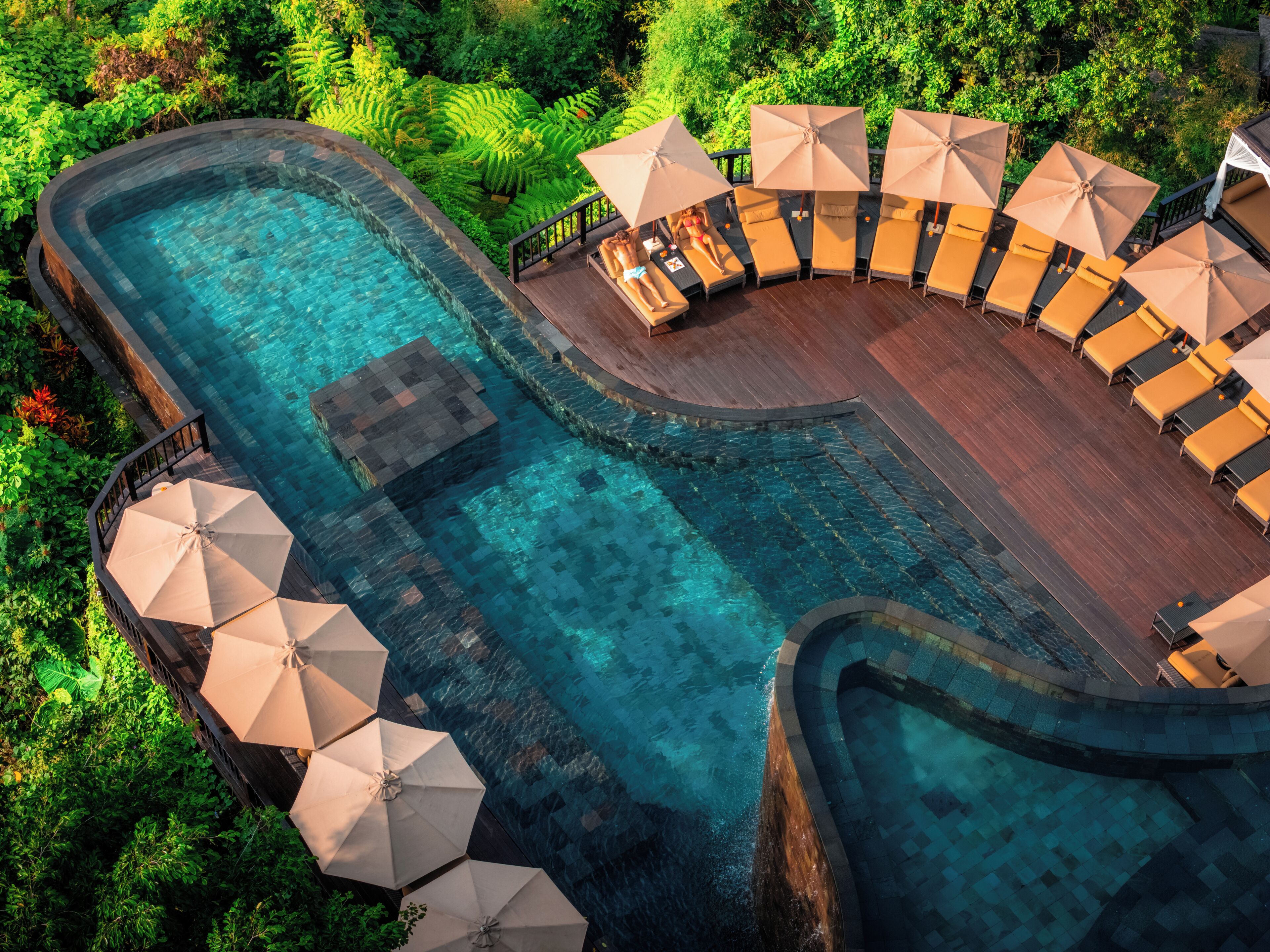 Piscina de un complejo turístico con agua cristalina, rodeada de sillas de descanso y sombrillas, ubicada en un entorno tropical exuberante.