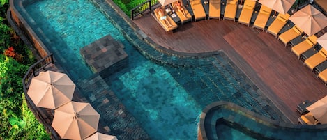 A resort pool with clear water, surrounded by lounge chairs and umbrellas, set in a lush, tropical environment.