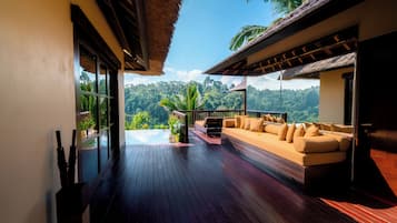 Terraza de madera con un sofá y una piscina pequeña, rodeada de abundante vegetación y vistas a la montaña.