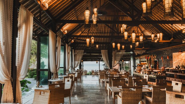 Un restaurante con mobiliario de mimbre, faroles colgantes y vistas al mar.