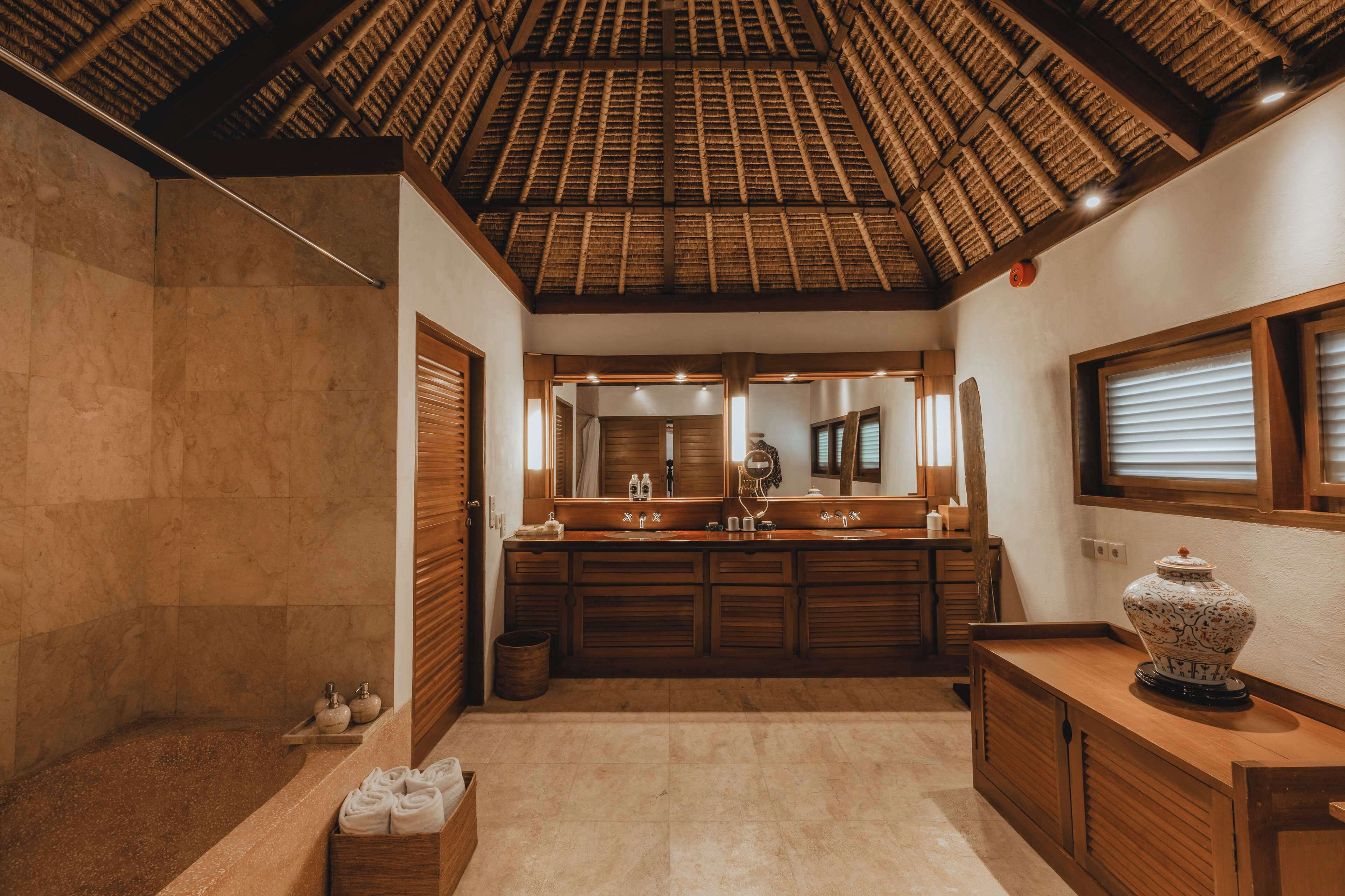 A bathroom with a large mirror, wooden cabinets, a bathtub, and a ceiling with a thatched design.