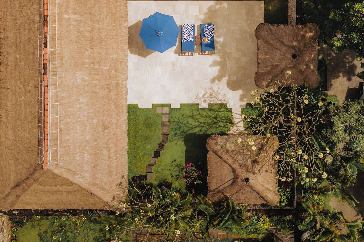 An aerial view of a resort with a swimming pool, lounge area, and lush vegetation.