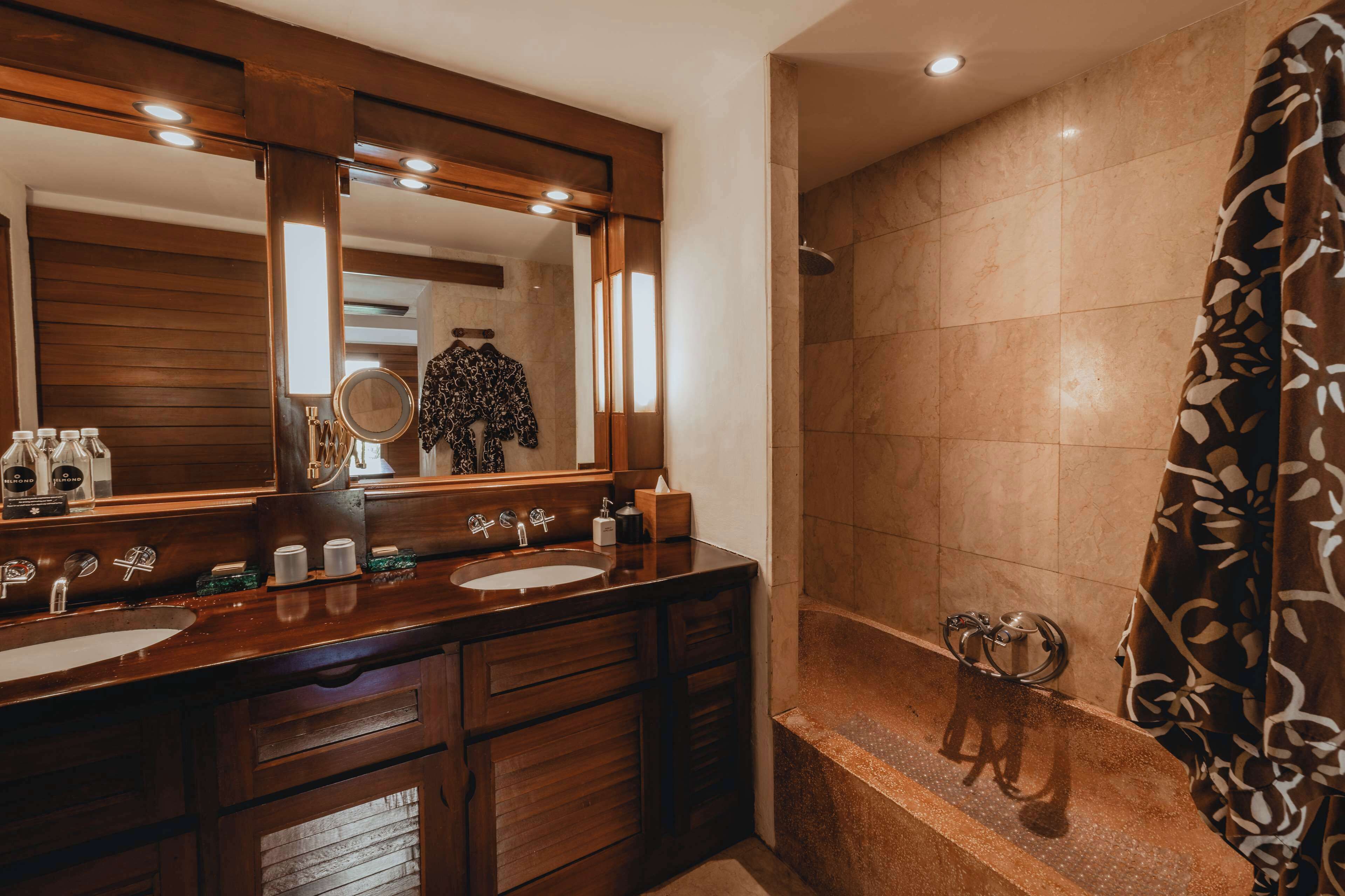 A bathroom with a wooden vanity, two sinks, a large mirror, and a shower area with a patterned shower curtain.