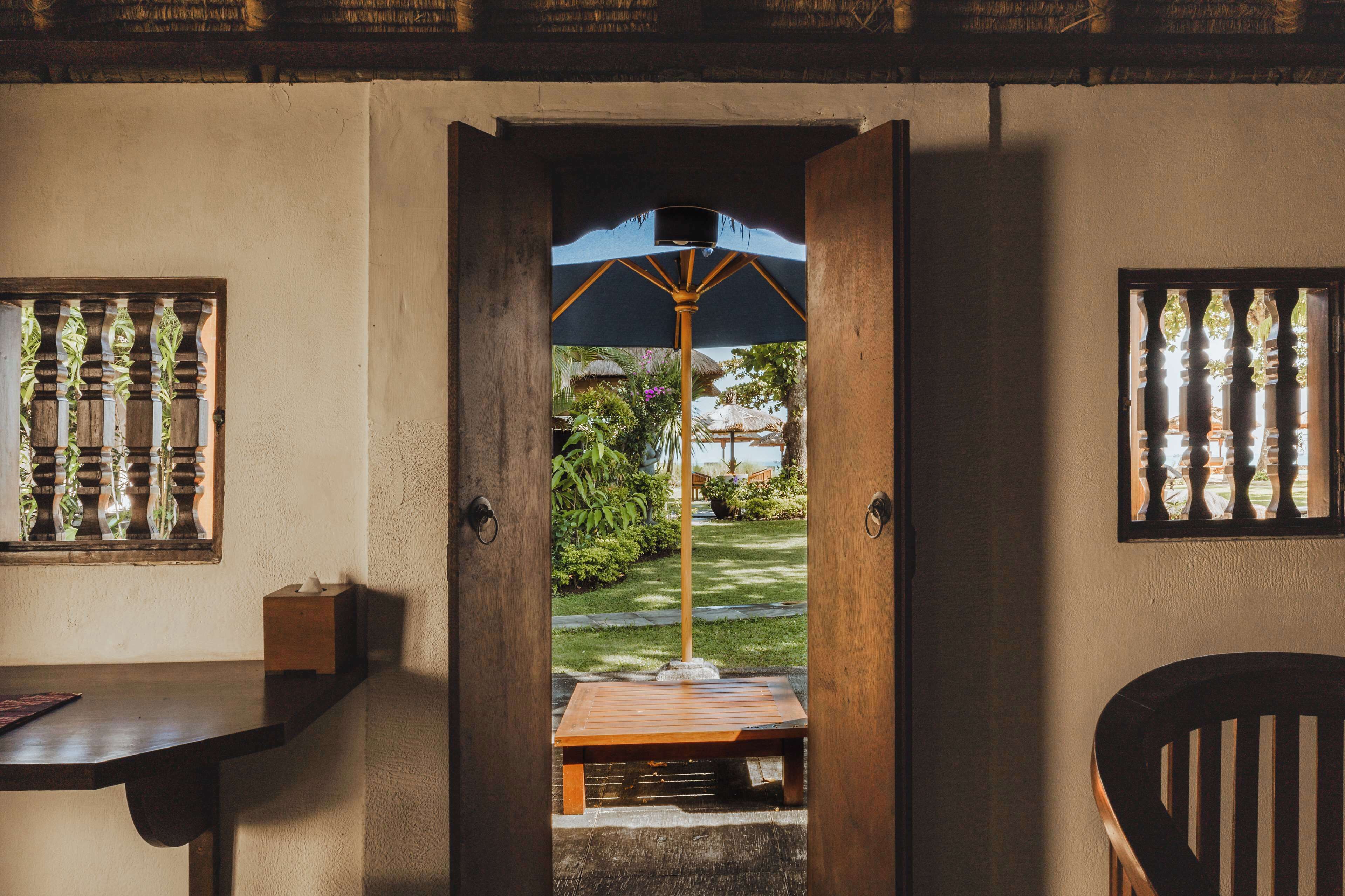 Una puerta que da a un jardín con un banco de madera y una mesa, y una silla visible a la derecha.