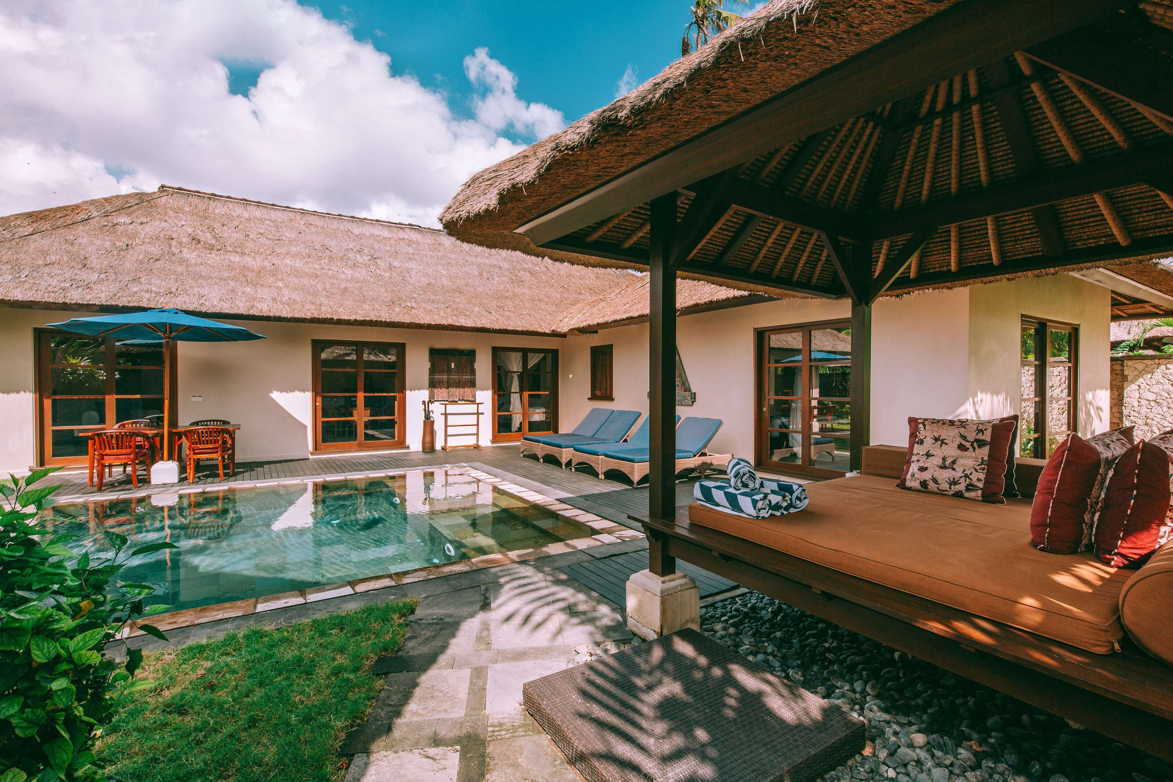 A pool area with lounge chairs, a thatched-roof structure, and a seating area with cushions.