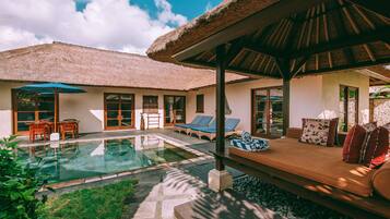 A pool area with lounge chairs, a thatched-roof structure, and a seating area with cushions.