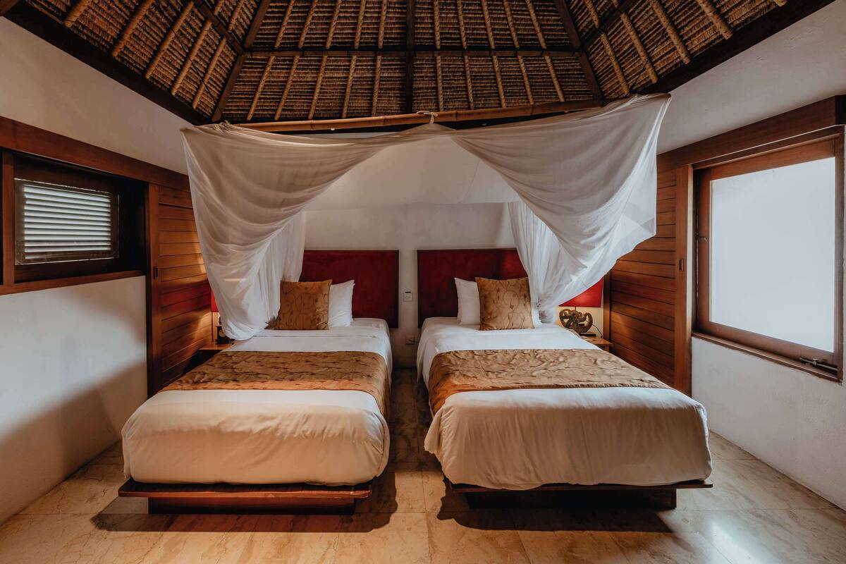 A room with two beds, a wooden ceiling, and a window.