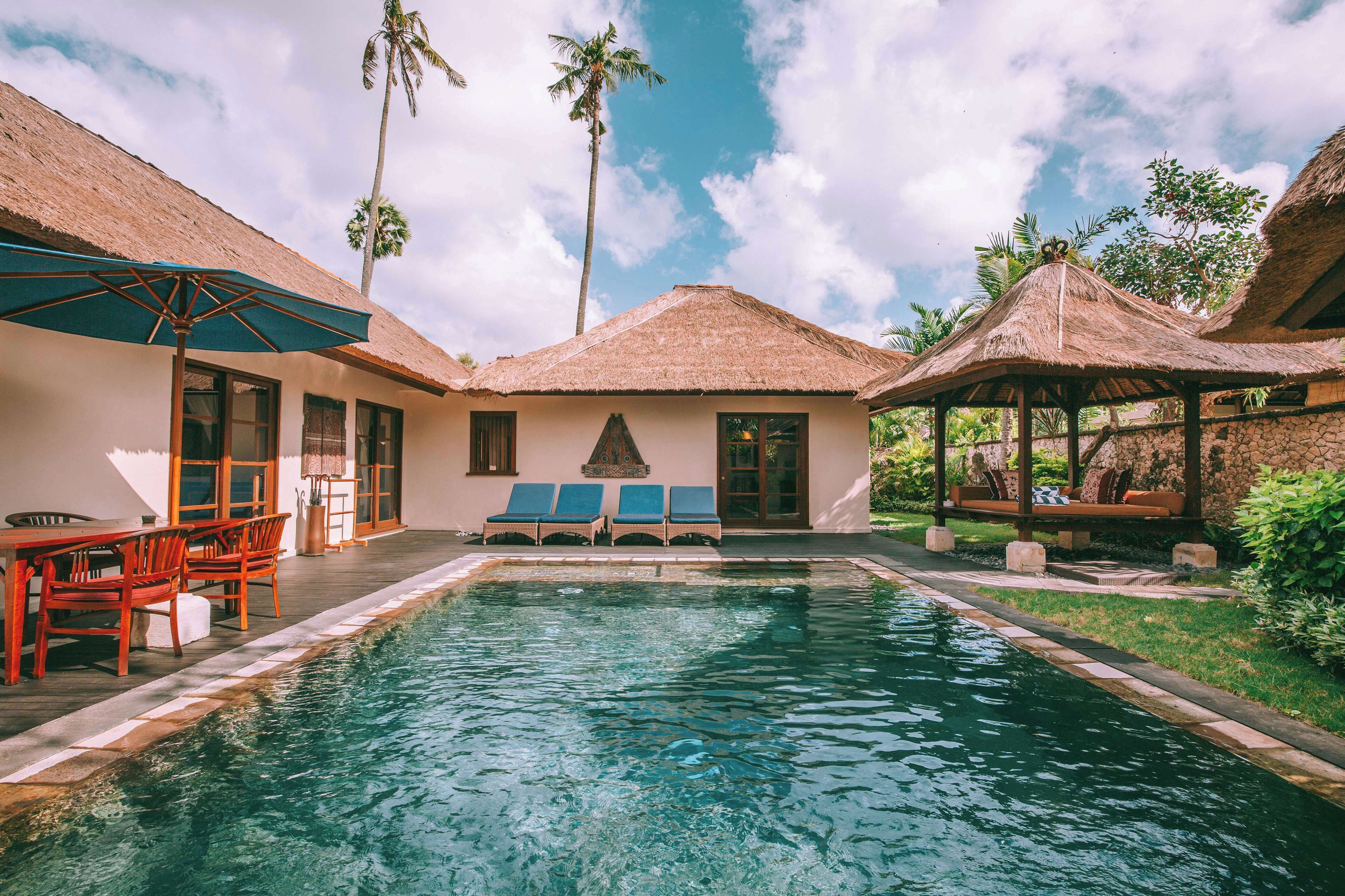 A pool area with lounge chairs, a table, and a thatched-roof structure.