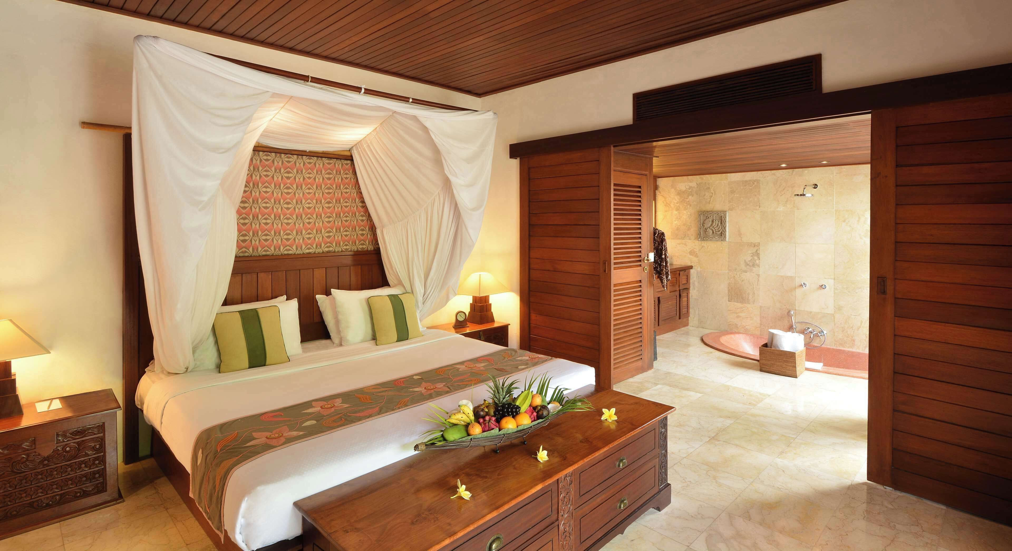 A bedroom with a bed, a bedside table, a fruit basket, and a bathroom with a sink and shower.